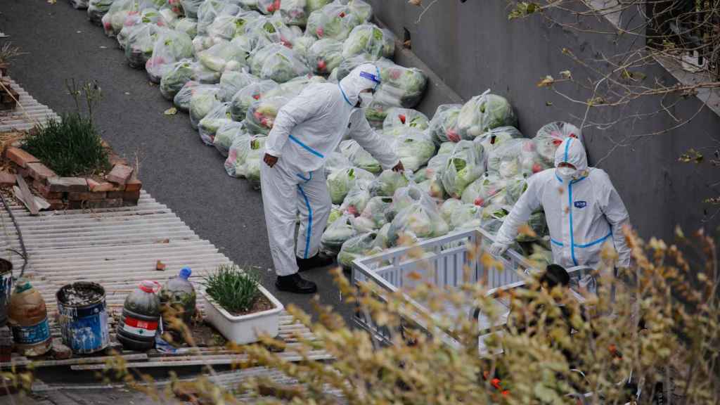Des agents d'assainissement préparent des sacs de légumes pour des résidents confinés à Pékin.
